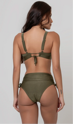 Uma mulher de costas, com cabelos escuros vestindo um biquíni verde. Top estruturado com aro e bojo, sendo um sutiã meia taça. A calcinha é de cintura alta hot pant com cordões laterais para amarração detalhados. O fundo é cinza neutro. 
