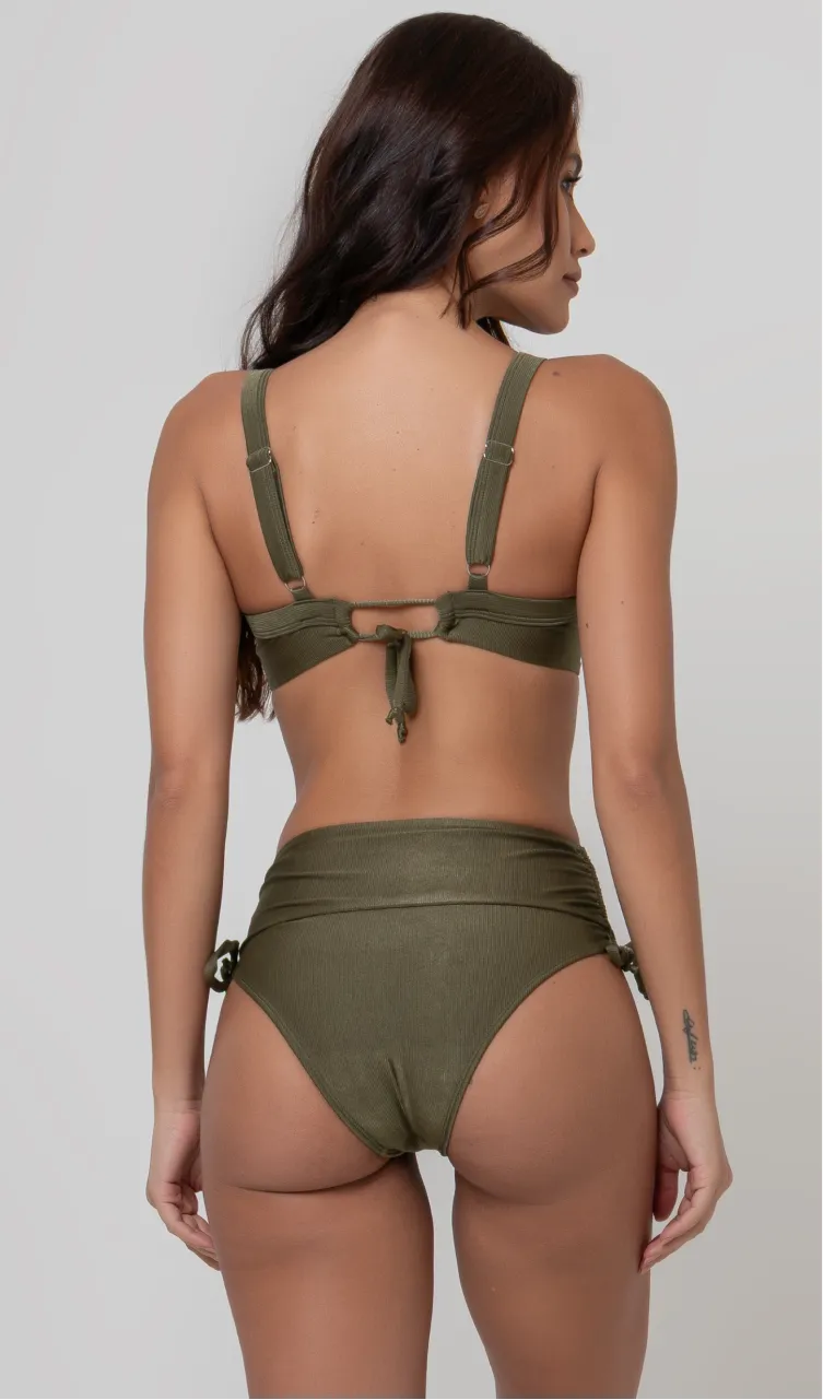 Uma mulher de costas, com cabelos escuros vestindo um biquíni verde. Top estruturado com aro e bojo, sendo um sutiã meia taça. A calcinha é de cintura alta hot pant com cordões laterais para amarração detalhados. O fundo é cinza neutro. 