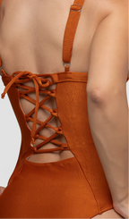 Modelo feminina de cabelos claros, de costas, em um estúdio com fundo neutro, vestindo um maiô cobre com efeito modelador. A peça é confeccionada em tecido de poliamida e elastano, com proteção solar. Maiô estruturado com sutiã meia taça com aro para sustentação, bojo, decote coração e amarração nas costas estilo espartilho.