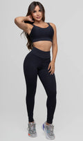 Modelo feminina, de frente, vestindo conjunto fitness feminino preto Mi Raromi, composto por top de alta sustentação com decote reto e calça legging de cintura alta. O conjunto possui tecido com proteção solar, ideal para garantir conforto, modelagem da silhueta e segurança durante os treinos. 