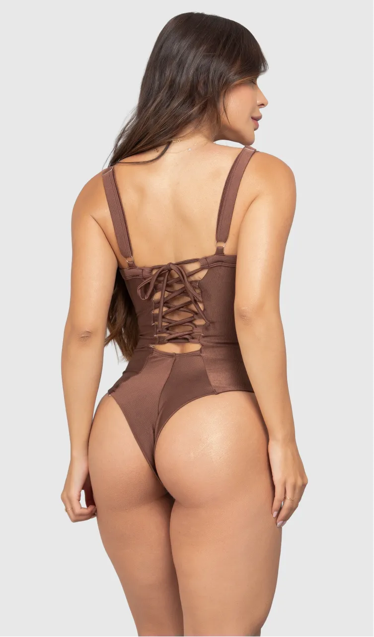 Modelo feminina de cabelos claros, de costas, em um estúdio com fundo neutro, vestindo um maiô marrom com efeito modelador. A peça é confeccionada em tecido de poliamida e elastano, com proteção solar. Maiô estruturado com sutiã meia taça com aro para sustentação, bojo, decote coração e amarração nas costas estilo espartilho.