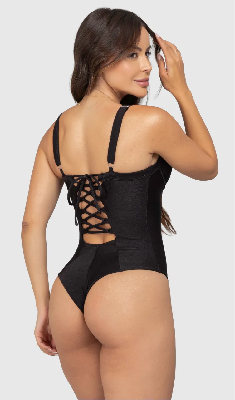 Modelo feminina de cabelos claros, de costas, em um estúdio com fundo neutro, vestindo um maiô preto com efeito modelador. A peça é confeccionada em tecido de poliamida e elastano, com proteção solar. Maiô estruturado com sutiã meia taça com aro para sustentação, bojo, decote coração e amarração nas costas estilo espartilho.