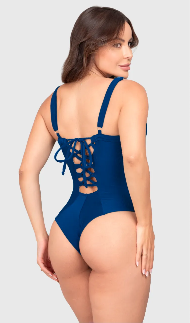 Modelo feminina de cabelos claros, de costas, em um estúdio com fundo neutro, vestindo um maiô azul marinho com efeito modelador. A peça é confeccionada em tecido de poliamida e elastano, com proteção solar. Maiô estruturado com sutiã meia taça com aro para sustentação, bojo, decote coração e amarração nas costas estilo espartilho.