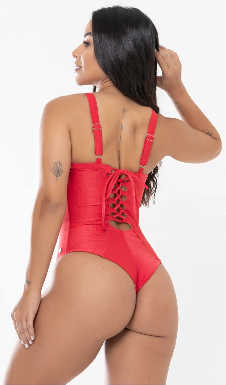 Modelo feminina de cabelos claros, de costas, em um estúdio com fundo neutro, vestindo um maiô vermelho melancia com efeito modelador. A peça é confeccionada em tecido de poliamida e elastano, com proteção solar. Maiô estruturado com sutiã meia taça com aro para sustentação, bojo, decote coração e amarração nas costas estilo espartilho.