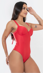 Modelo feminina de cabelos claros, de lado, em um estúdio com fundo neutro, vestindo um maiô vermelho melancia com efeito modelador. A peça é confeccionada em tecido de poliamida e elastano, com proteção solar. Maiô estruturado com sutiã meia taça com aro para sustentação, bojo, decote coração e amarração nas costas estilo espartilho.