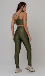 Uma foto de estúdio de corpo inteiro de uma mulher jovem posando de costas com um conjunto fitness feminino feito de poliamida e elastano na cor verde. O conjunto é composto por um top de alças finas, bojo removível e uma calça legging de cintura alta com bolsos laterais práticos. Ela está com uma mão no bolso da legging e usa tênis esportivos cinzas e bege. O fundo é cinza claro e bem iluminado. Este conjunto de treino preto é ideal para academia e exercícios físicos.