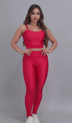 Vídeo de modelo feminina usando conjunto fitness feminino vermelho Mi Raromi de duas peças. Inclui um top cropped de alcinhas finas e leggings de cintura alta correspondentes, ambos feitos de poliamida e elastano. A modelo está em pé contra um fundo cinza neutro, usando tênis brancos.